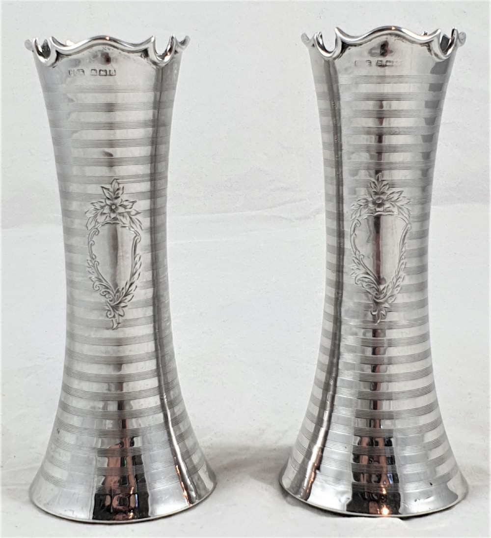 A pair of slender sterling silver trumpet vases featuring scalloped rims, horizontal reeded decoration, and central engraved floral cartouches.