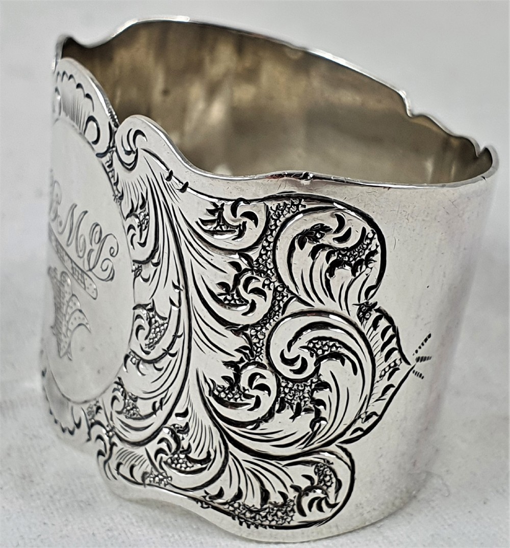 A Victorian silver napkin ring featuring a scalloped rim, detailed scroll engraving, and a central circular cartouche with a monogram. View II