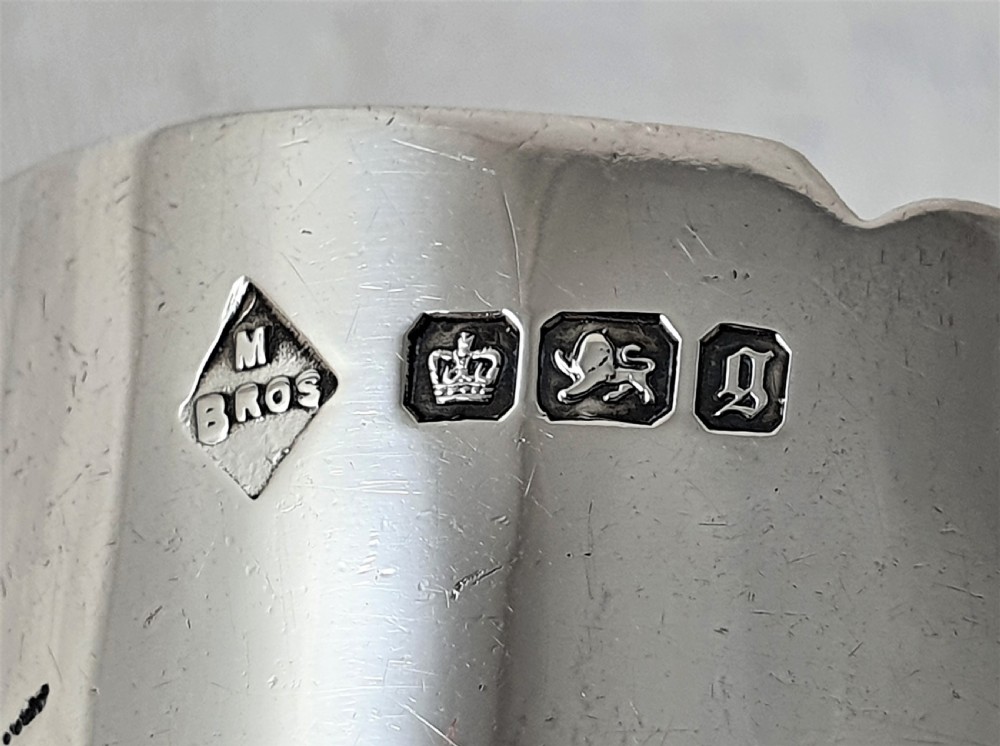 A Victorian silver napkin ring featuring a scalloped rim, detailed scroll engraving, and a central circular cartouche with a monogram. View VI
