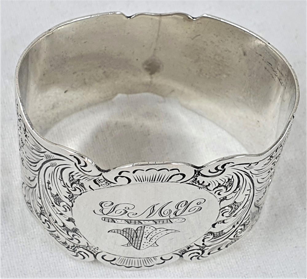 A Victorian silver napkin ring featuring a scalloped rim, detailed scroll engraving, and a central circular cartouche with a monogram. View VII