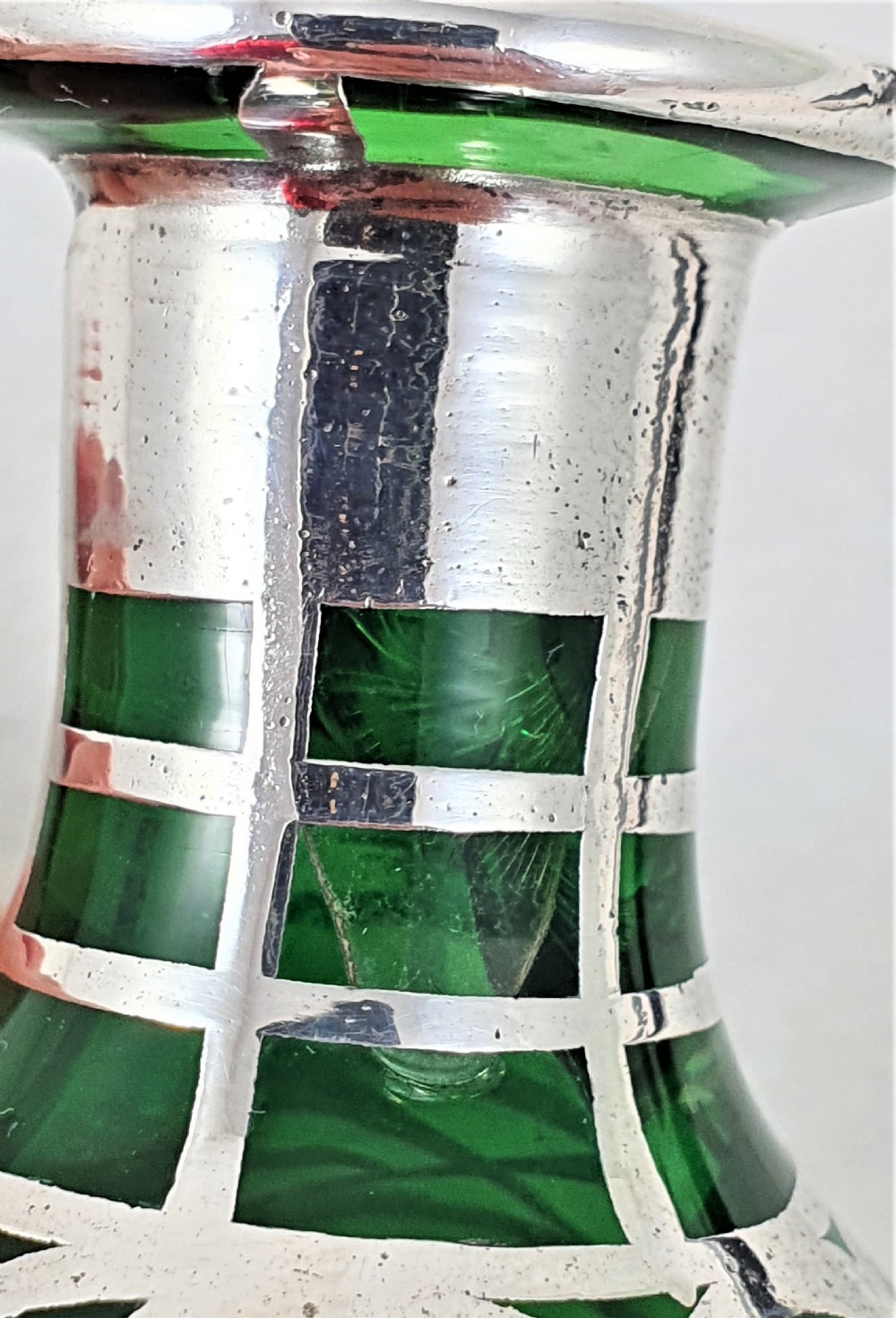 An emerald green glass perfume bottle featuring silver overlay in geometric and linear patterns with a matching silver-covered globe stopper. View X