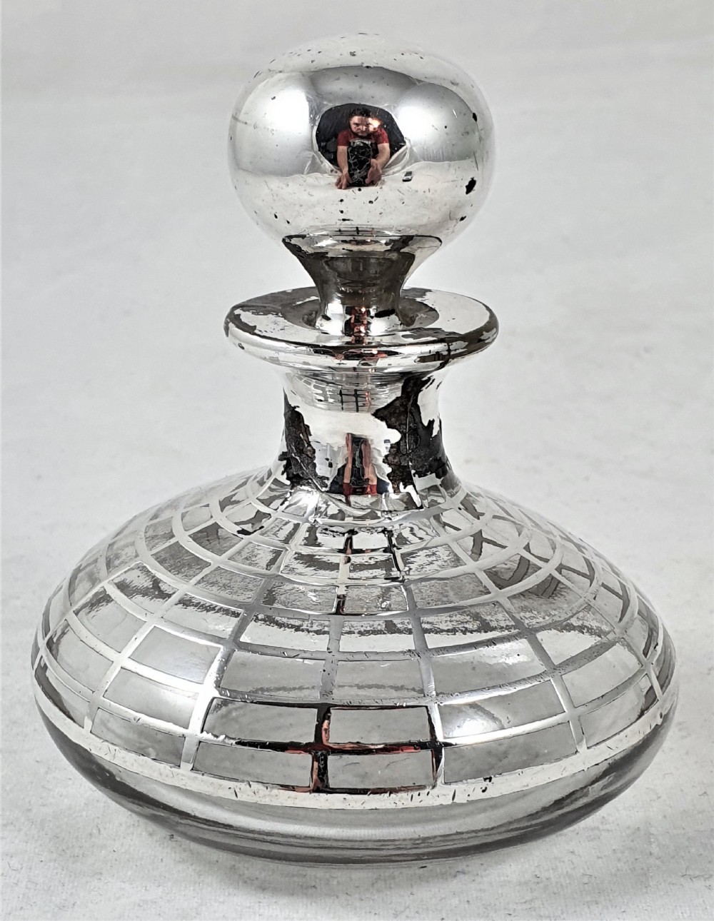 A round clear glass perfume bottle featuring a grid pattern silver overlay and a spherical silver stopper. View III