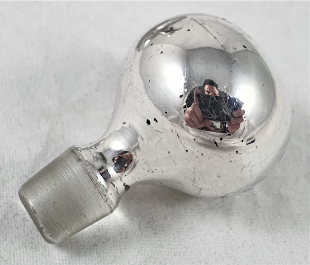 A round clear glass perfume bottle featuring a grid pattern silver overlay and a spherical silver stopper. View VI