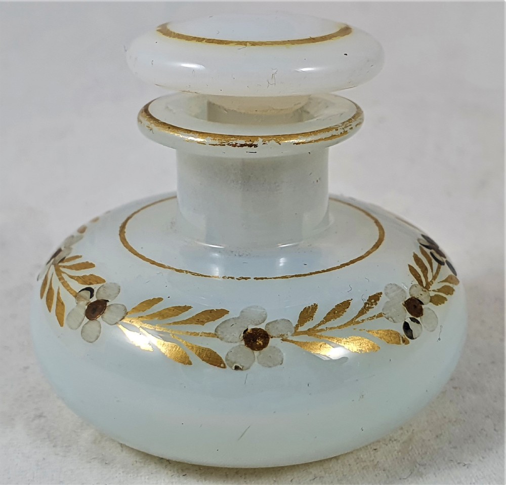 A small squat opalescent glass scent bottle featuring hand-painted gilded floral garlands around the body and a matching disc stopper.
