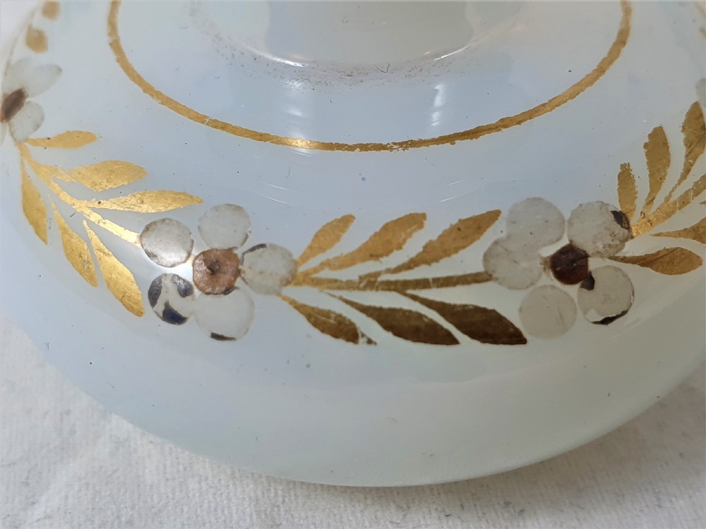 A small squat opalescent glass scent bottle featuring hand-painted gilded floral garlands around the body and a matching disc stopper. View V