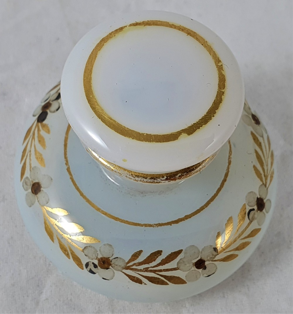 A small squat opalescent glass scent bottle featuring hand-painted gilded floral garlands around the body and a matching disc stopper. View VI