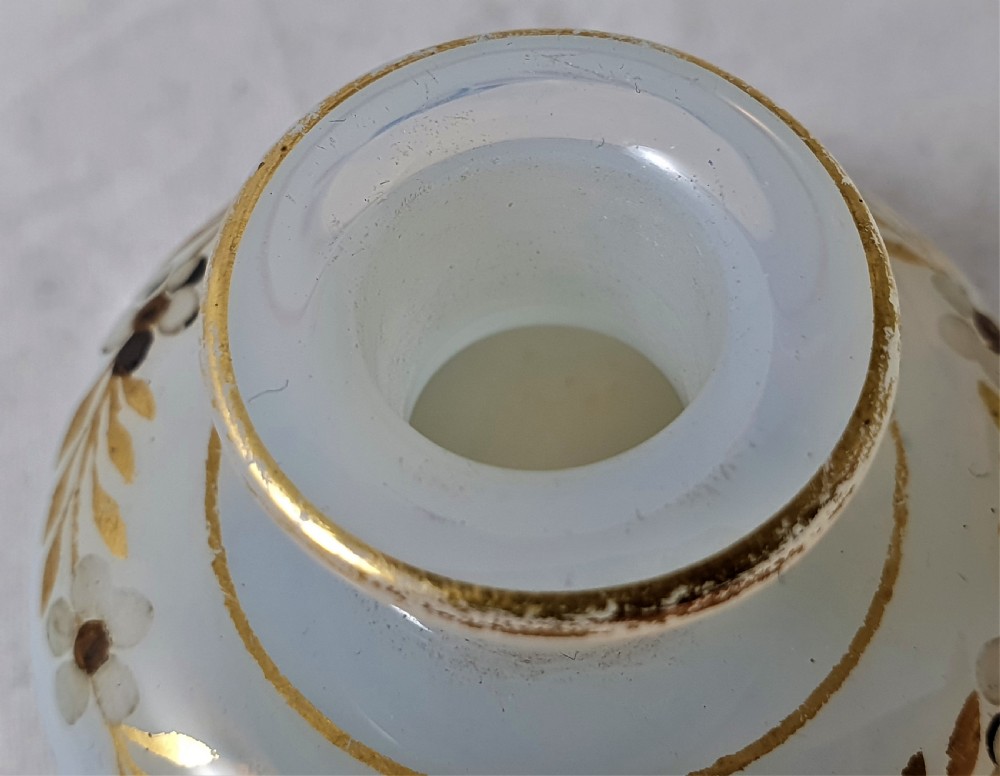 A small squat opalescent glass scent bottle featuring hand-painted gilded floral garlands around the body and a matching disc stopper. View VII