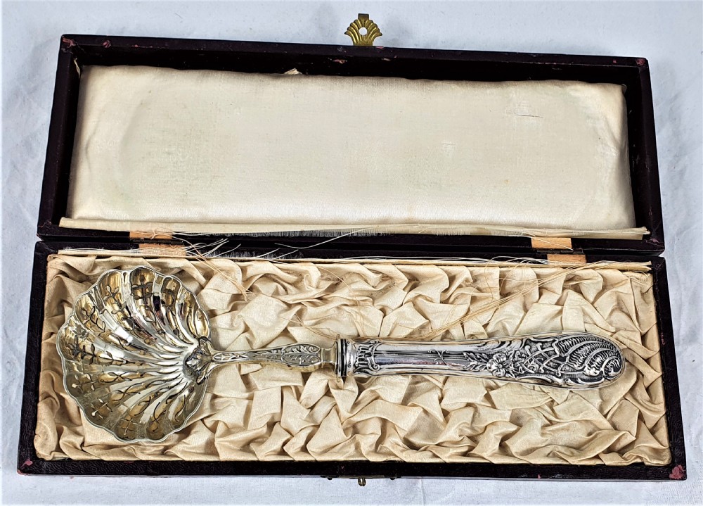A nineteenth-century French silver-plated sugar sifter featuring a pierced shell-shaped gilded bowl and relief handle, presented in a dark fitted case.