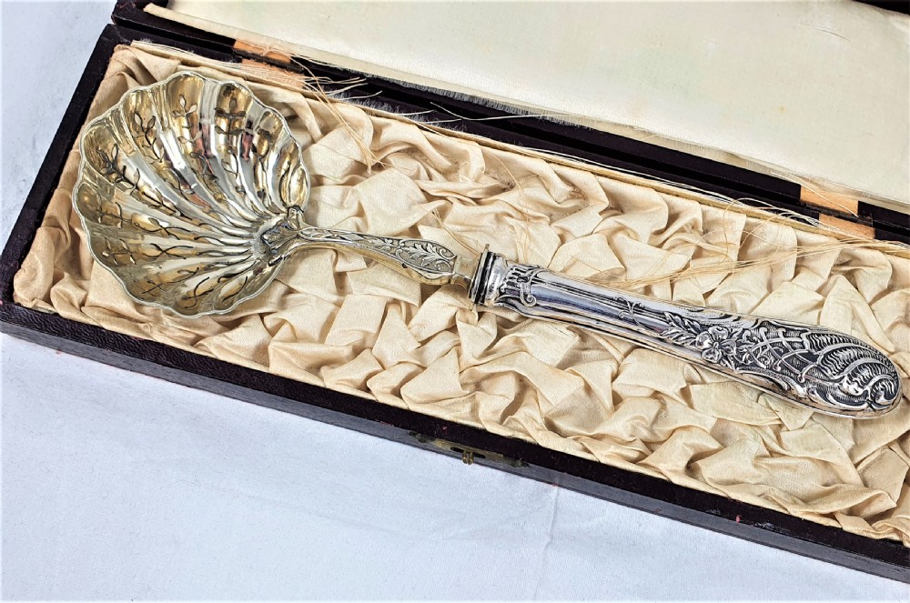 A nineteenth-century French silver-plated sugar sifter featuring a pierced shell-shaped gilded bowl and relief handle, presented in a dark fitted case. View II