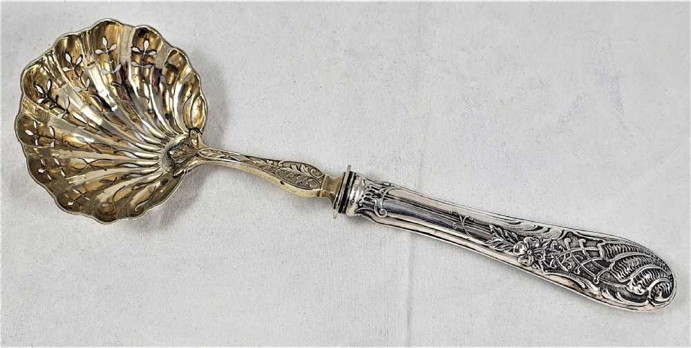 A nineteenth-century French silver-plated sugar sifter featuring a pierced shell-shaped gilded bowl and relief handle, presented in a dark fitted case. View III