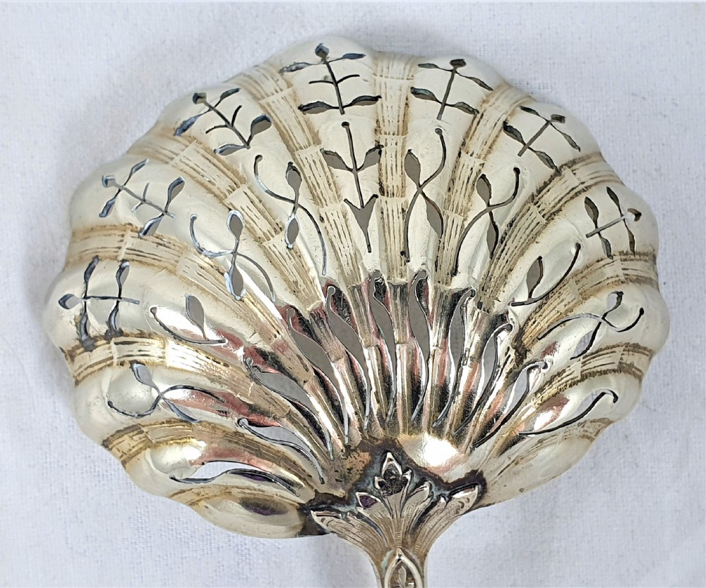 A nineteenth-century French silver-plated sugar sifter featuring a pierced shell-shaped gilded bowl and relief handle, presented in a dark fitted case. View IX