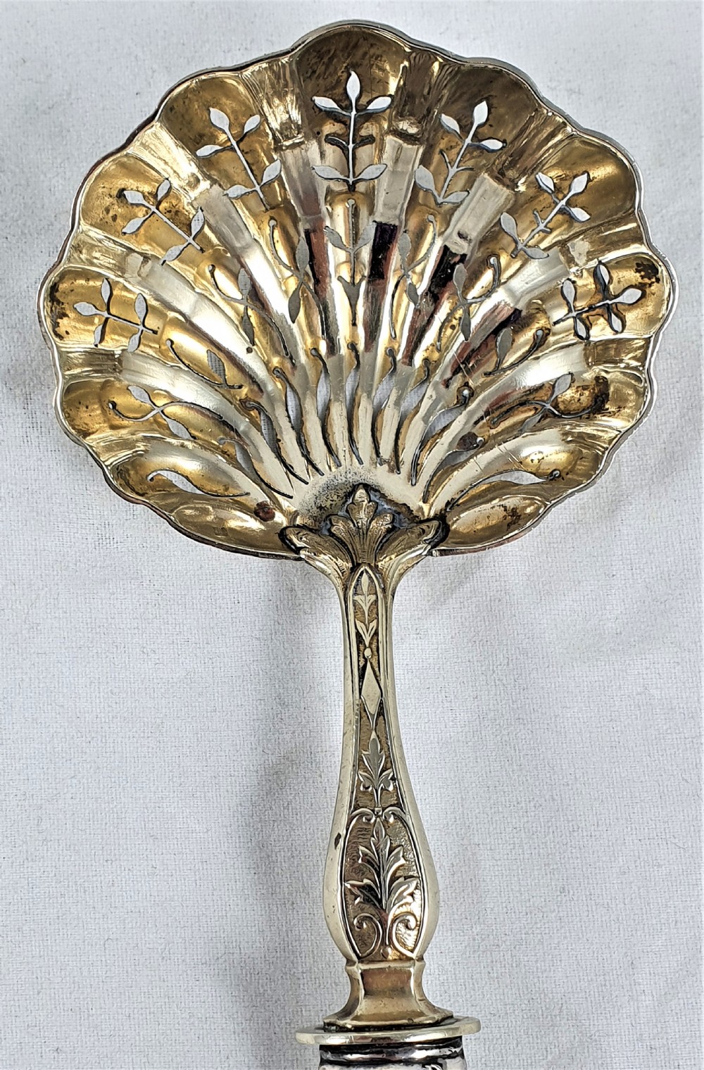 A nineteenth-century French silver-plated sugar sifter featuring a pierced shell-shaped gilded bowl and relief handle, presented in a dark fitted case. View XI