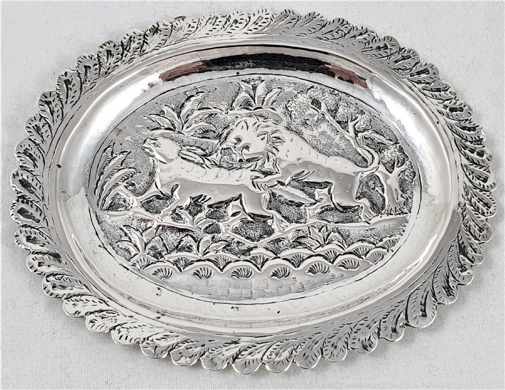 An oval silver dish featuring a chased repousse hunting scene in relief with a leaf pattern border.