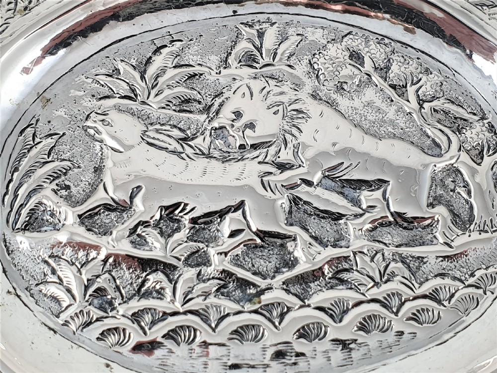 An oval silver dish featuring a chased repousse hunting scene in relief with a leaf pattern border. View II