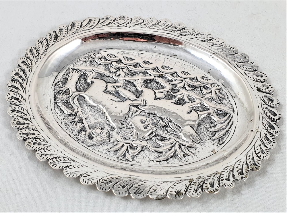 An oval silver dish featuring a chased repousse hunting scene in relief with a leaf pattern border. View III