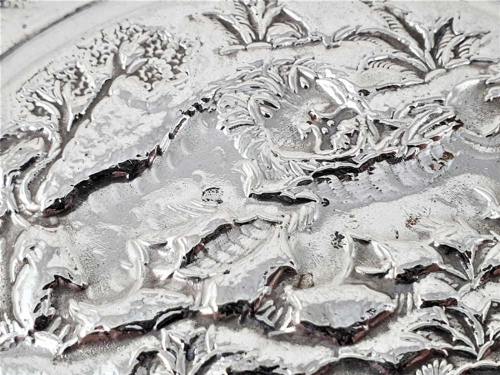 An oval silver dish featuring a chased repousse hunting scene in relief with a leaf pattern border. View VI