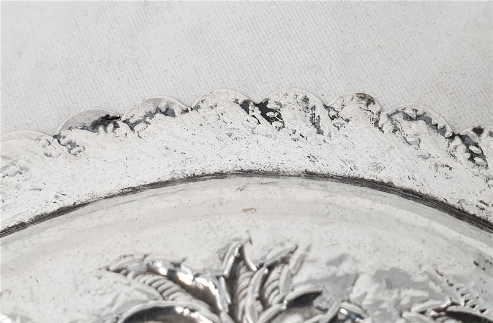 An oval silver dish featuring a chased repousse hunting scene in relief with a leaf pattern border. View VII