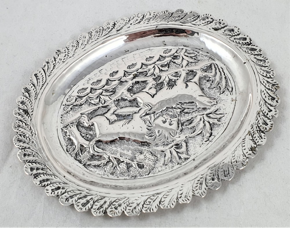An oval silver dish featuring a chased repousse hunting scene in relief with a leaf pattern border. View VIII