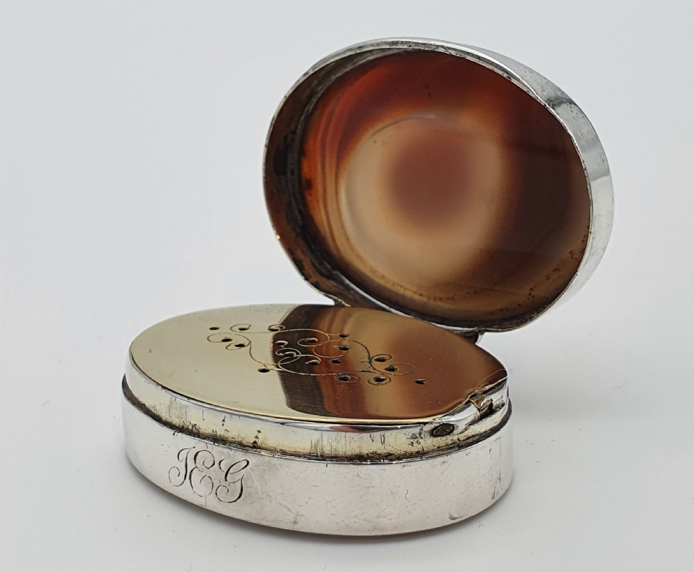 A Georgian oval silver vinaigrette featuring a smooth brown agate top and engraved script monogram on the silver collar. View V