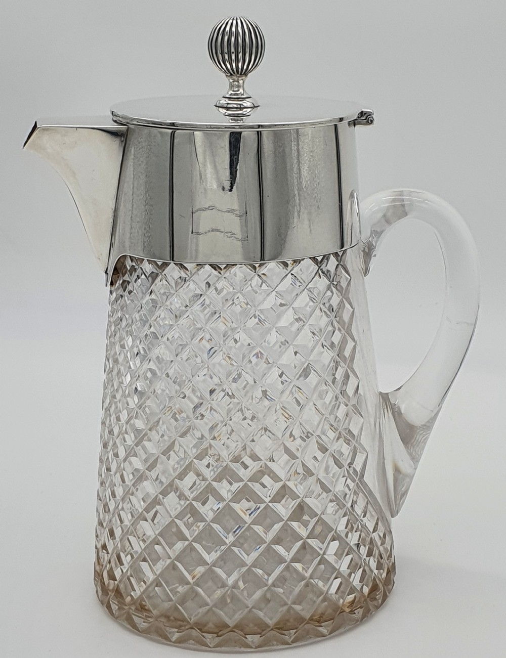 A late Victorian claret jug featuring a diamond-cut clear glass body paired with a polished sterling silver collar, hinged flat lid, fluted finial, and clear glass handle. View III