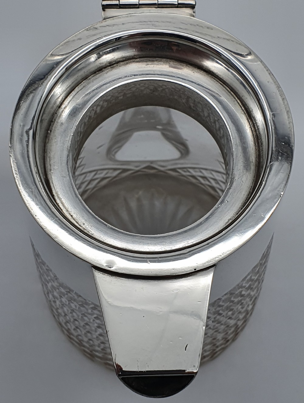 A late Victorian claret jug featuring a diamond-cut clear glass body paired with a polished sterling silver collar, hinged flat lid, fluted finial, and clear glass handle. View X