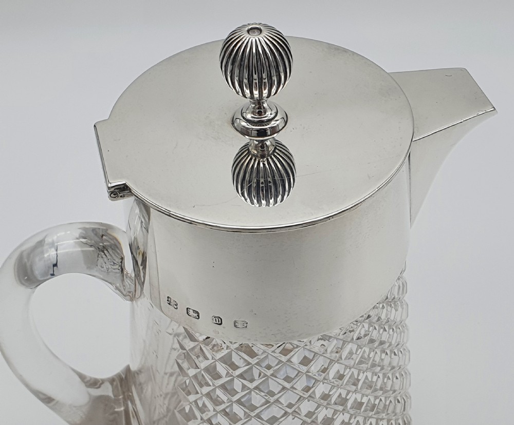 A late Victorian claret jug featuring a diamond-cut clear glass body paired with a polished sterling silver collar, hinged flat lid, fluted finial, and clear glass handle. View XII