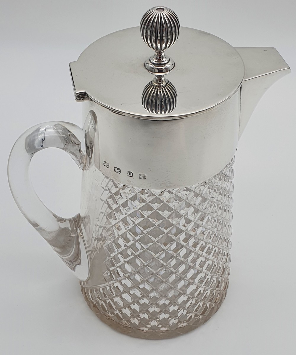 A late Victorian claret jug featuring a diamond-cut clear glass body paired with a polished sterling silver collar, hinged flat lid, fluted finial, and clear glass handle. View XIII