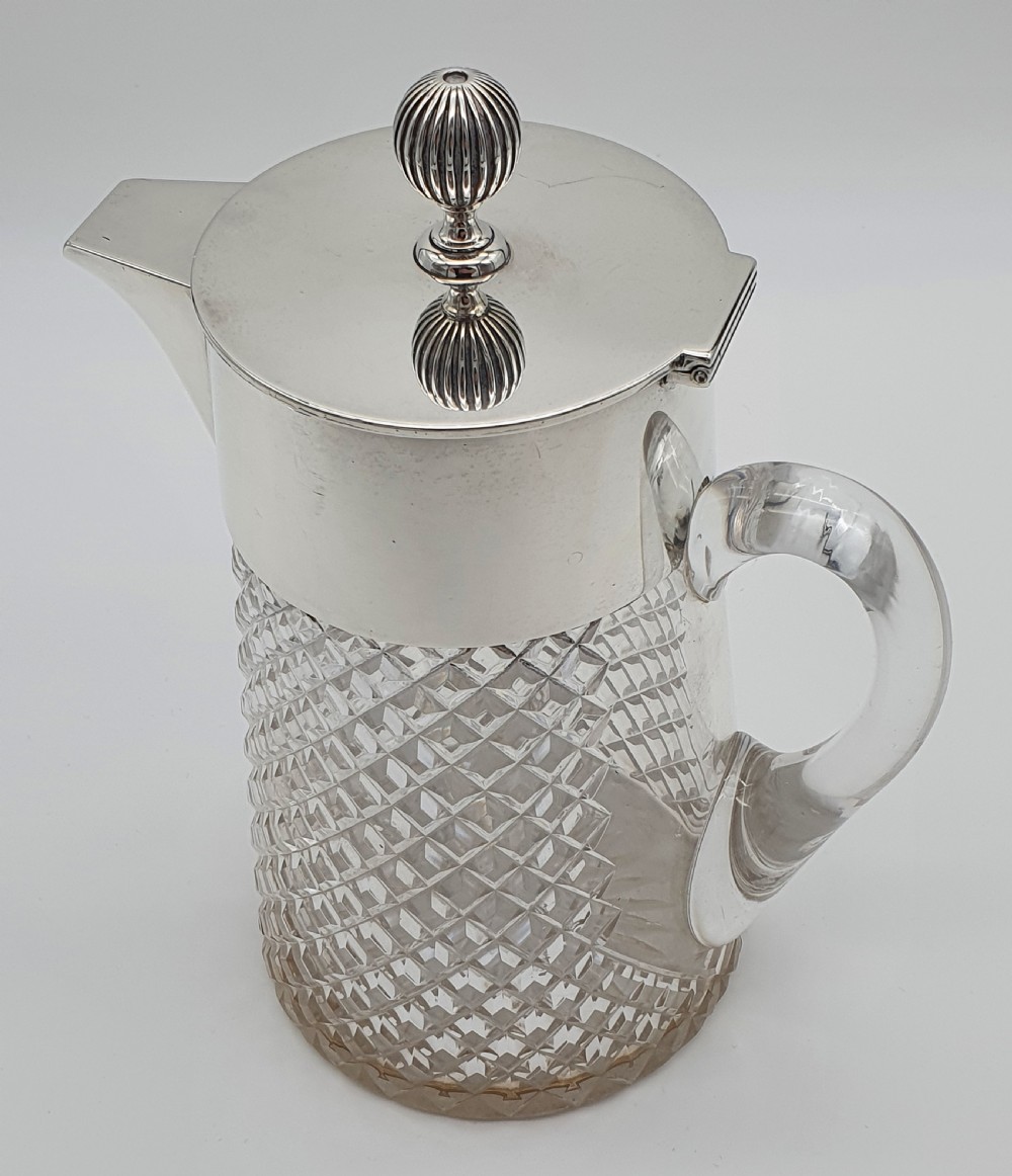 A late Victorian claret jug featuring a diamond-cut clear glass body paired with a polished sterling silver collar, hinged flat lid, fluted finial, and clear glass handle. View XIV