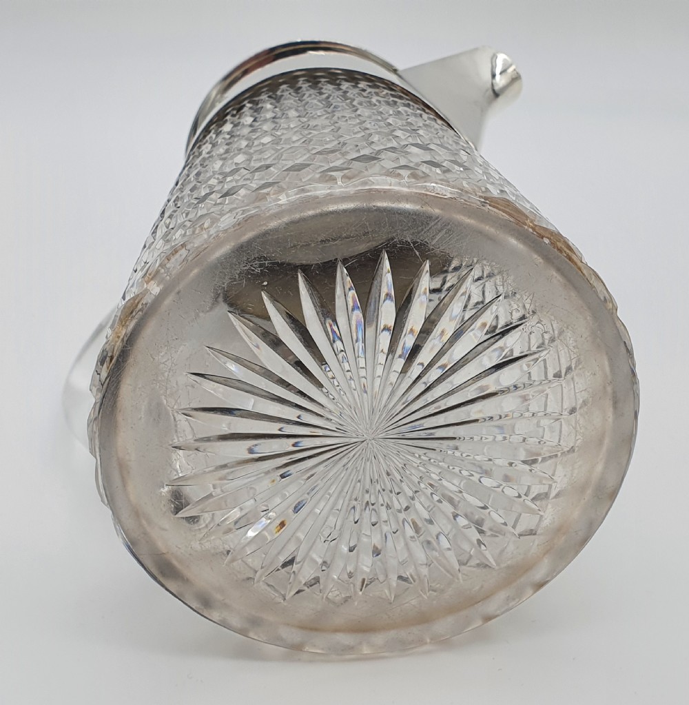 A late Victorian claret jug featuring a diamond-cut clear glass body paired with a polished sterling silver collar, hinged flat lid, fluted finial, and clear glass handle. View XV