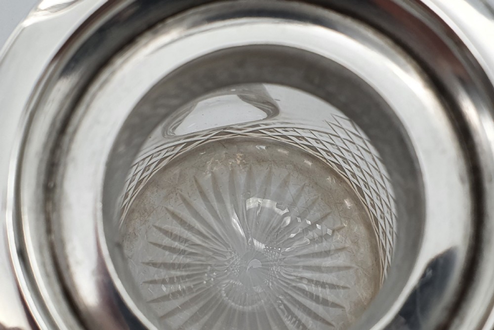A late Victorian claret jug featuring a diamond-cut clear glass body paired with a polished sterling silver collar, hinged flat lid, fluted finial, and clear glass handle. View XVII