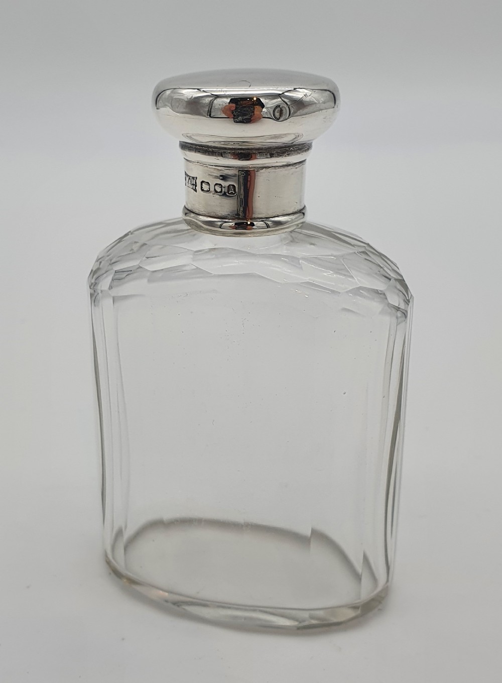 A George V clear faceted glass bottle featuring a hallmarked sterling silver collar and polished silver top cap.