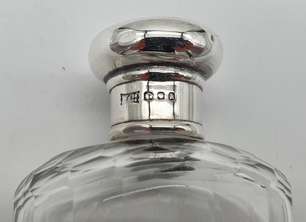 A George V clear faceted glass bottle featuring a hallmarked sterling silver collar and polished silver top cap. View IX