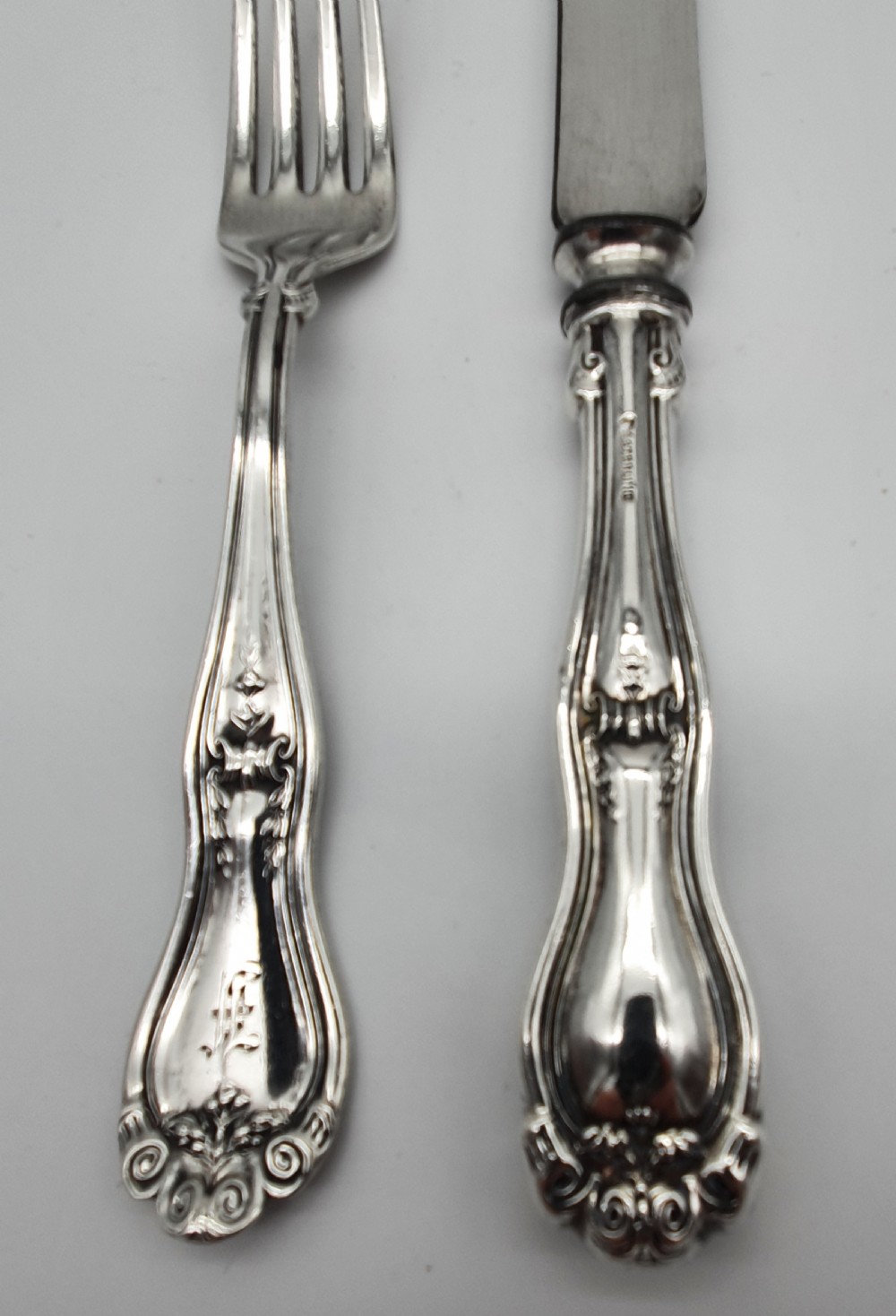 An American sterling silver table knife and matching four-tined fork featuring ornate foliate scrollwork handles. View V