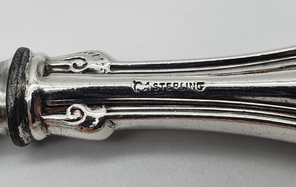 An American sterling silver table knife and matching four-tined fork featuring ornate foliate scrollwork handles. View X