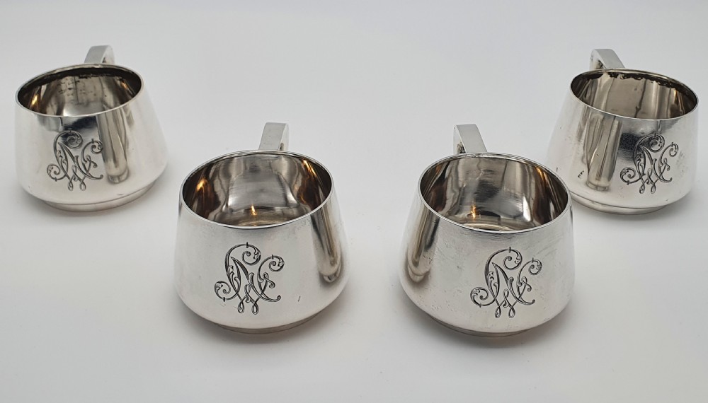 A set of four small silver vodka cups with angular handles and engraved monograms against a white backdrop. View II