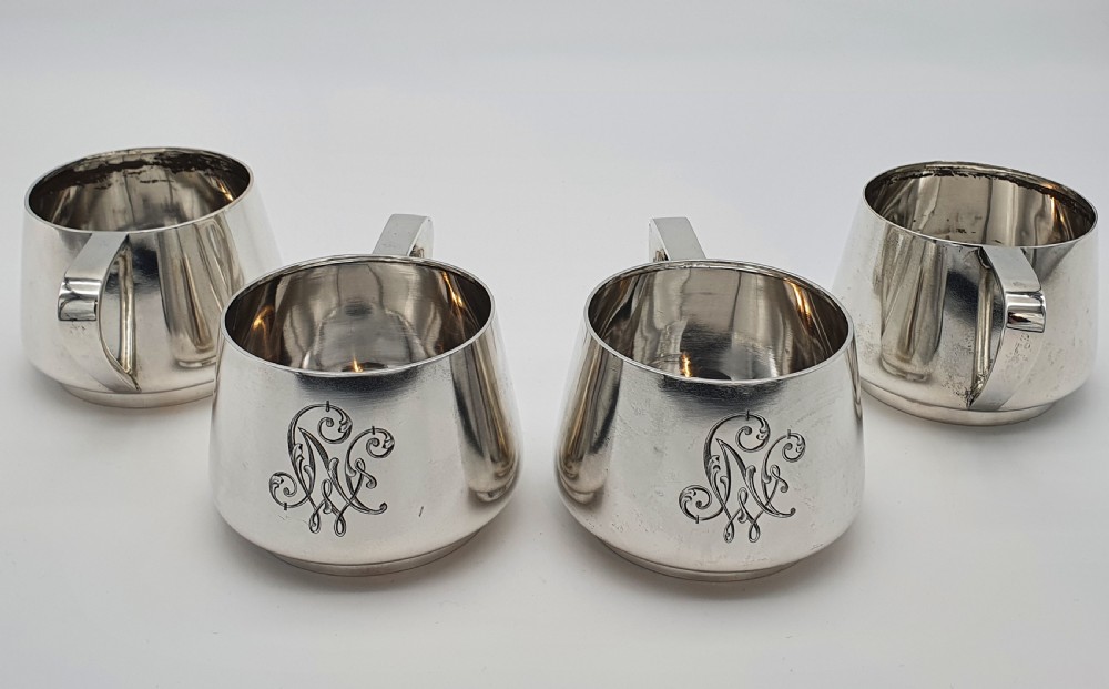 A set of four small silver vodka cups with angular handles and engraved monograms against a white backdrop. View III