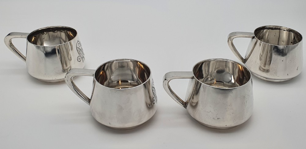 A set of four small silver vodka cups with angular handles and engraved monograms against a white backdrop. View IV