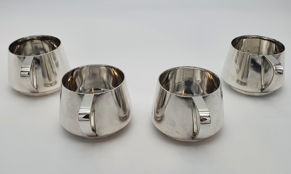A set of four small silver vodka cups with angular handles and engraved monograms against a white backdrop. View V