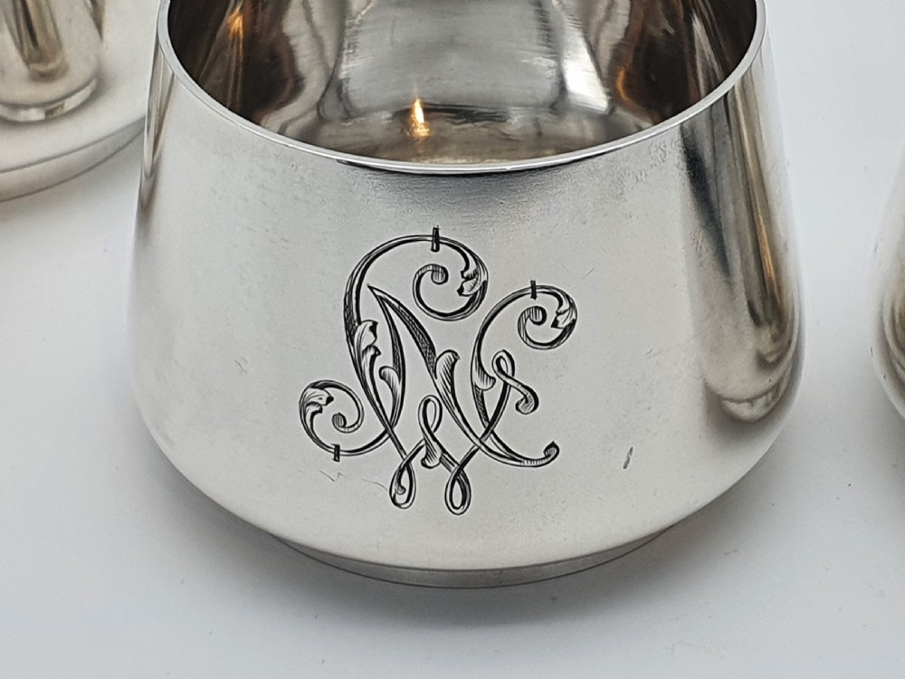 A set of four small silver vodka cups with angular handles and engraved monograms against a white backdrop. View VI