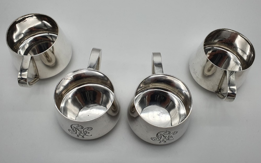 A set of four small silver vodka cups with angular handles and engraved monograms against a white backdrop. View VII