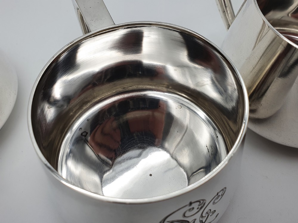 A set of four small silver vodka cups with angular handles and engraved monograms against a white backdrop. View X