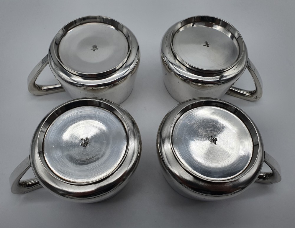 A set of four small silver vodka cups with angular handles and engraved monograms against a white backdrop. View XII
