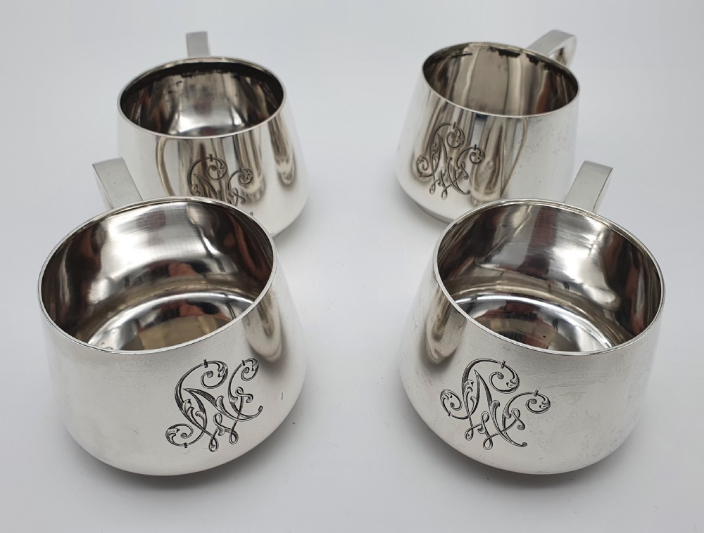 A set of four small silver vodka cups with angular handles and engraved monograms against a white backdrop. View XIX