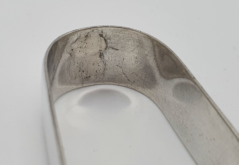 A pair of George III sterling silver sugar tongs featuring smooth spoon-shaped bowls and a curved bow hinge with makers mark TP. View III