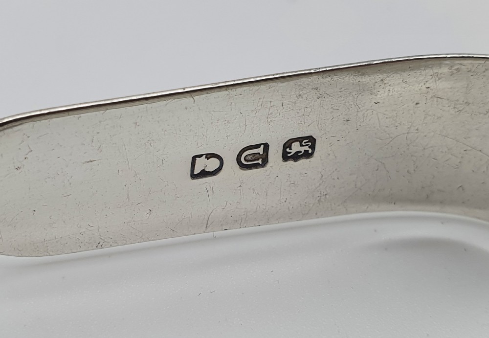 A pair of George III sterling silver sugar tongs featuring smooth spoon-shaped bowls and a curved bow hinge with makers mark TP. View VII