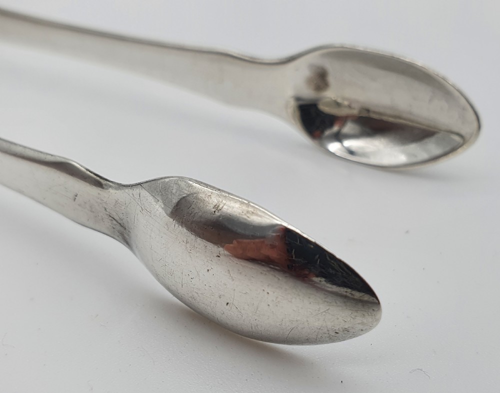 A pair of George III sterling silver sugar tongs featuring smooth spoon-shaped bowls and a curved bow hinge with makers mark TP. View X