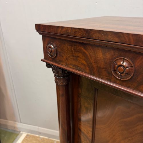 fig 1. A Late Regency flame mahogany pier cabinet featuring carved rosette medallions on the upper frieze, flanking side columns with carved capitals, and a single solid wood door.