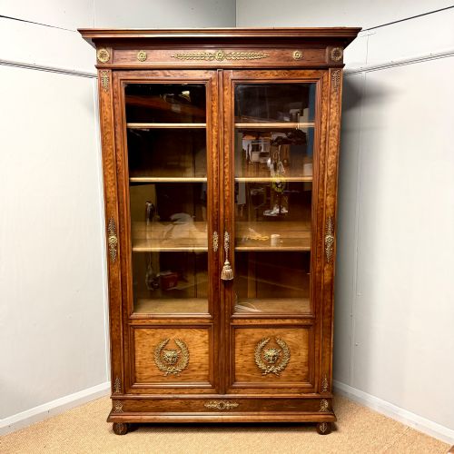 fig 1. A tall French Empire style warm brown timber bookcase featuring two glass-fronted doors, gilt brass laurel wreath mounts, and adjustable interior shelves.
