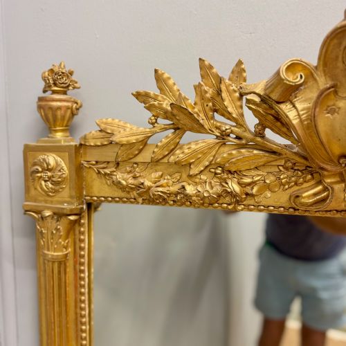 fig 1. A large rectangular French Louis XVI style water gilded mirror featuring fluted side pilasters and an elaborate carved crest with laurel leaves and urn finials.