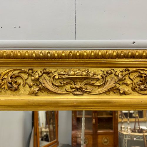 fig 3. A large horizontal rectangular mirror featuring an intricately carved giltwood frame with classical urn, floral, and leaf motifs.